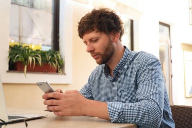 Kafedeki masada akıllı telefon kullanan yakışıklı adam.