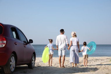 Plajda arabanın yanında şişme halkaları olan bir aile.