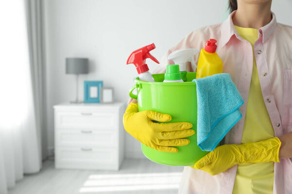 Woman holding bucket with different cleaning supplies at home, closeup. Space for text