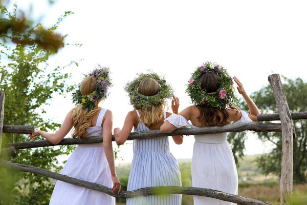 Молодые женщины носят венки из красивых цветов возле деревянного забора, вид сзади