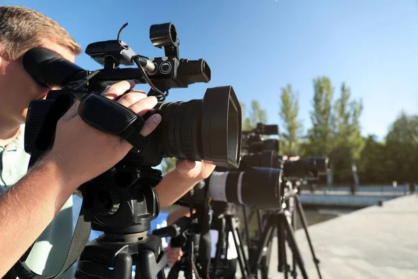 Operators with professional video cameras working outdoors on sunny day