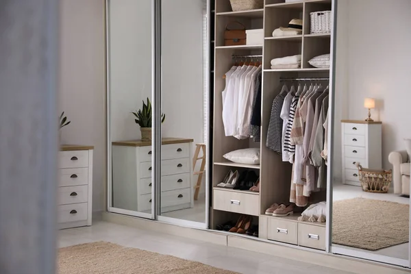 Wardrobe closet with different stylish clothes, shoes and home stuff in room