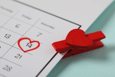 Üzerinde Sevgililer Günü yazan takvim ve turkuaz arka planda kırmızı mandal, yakın plan.