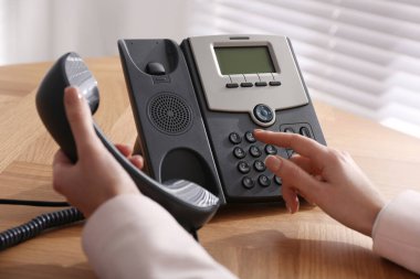Ofisteki ahşap masada masaüstü telefonu kullanan bir kadın, yakın plan. Yardım hattı servisi
