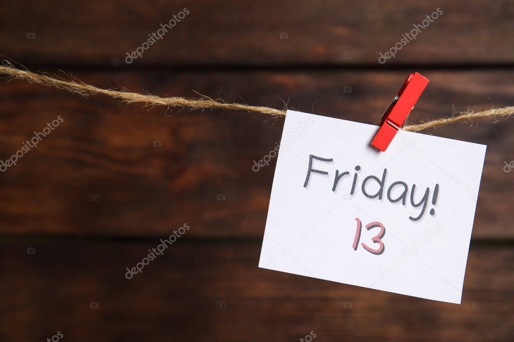 Paper note with phrase Friday! 13 hanging on twine against wooden background, space for text. Bad luck superstition