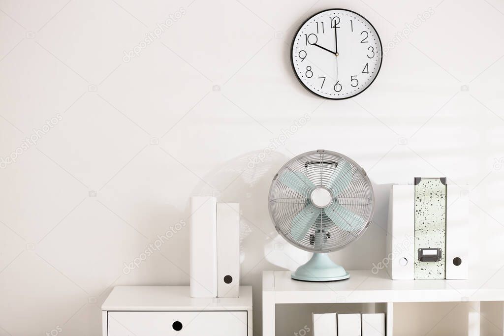 Modern electric fan on shelving unit in office. Space for text