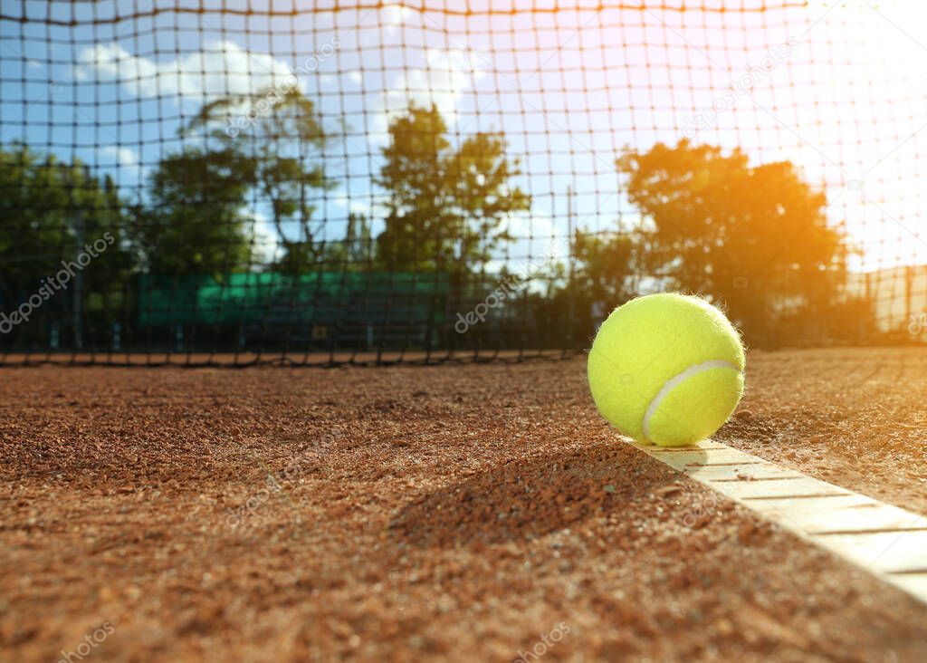 Bright yellow tennis ball on clay court. Space for text