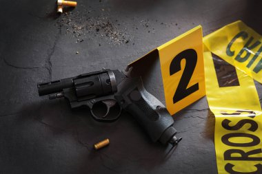 Siyah tahta üzerinde silah ve mermi kovanı olan bir kompozisyon. Suç mahalli