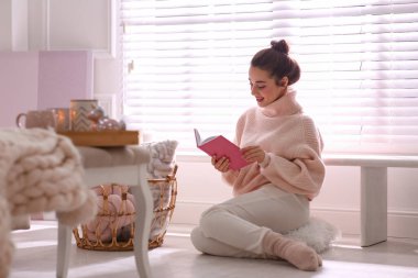 Evde kitap okuyarak rahatlayan güzel genç bir kadın. Sıcak atmosfer