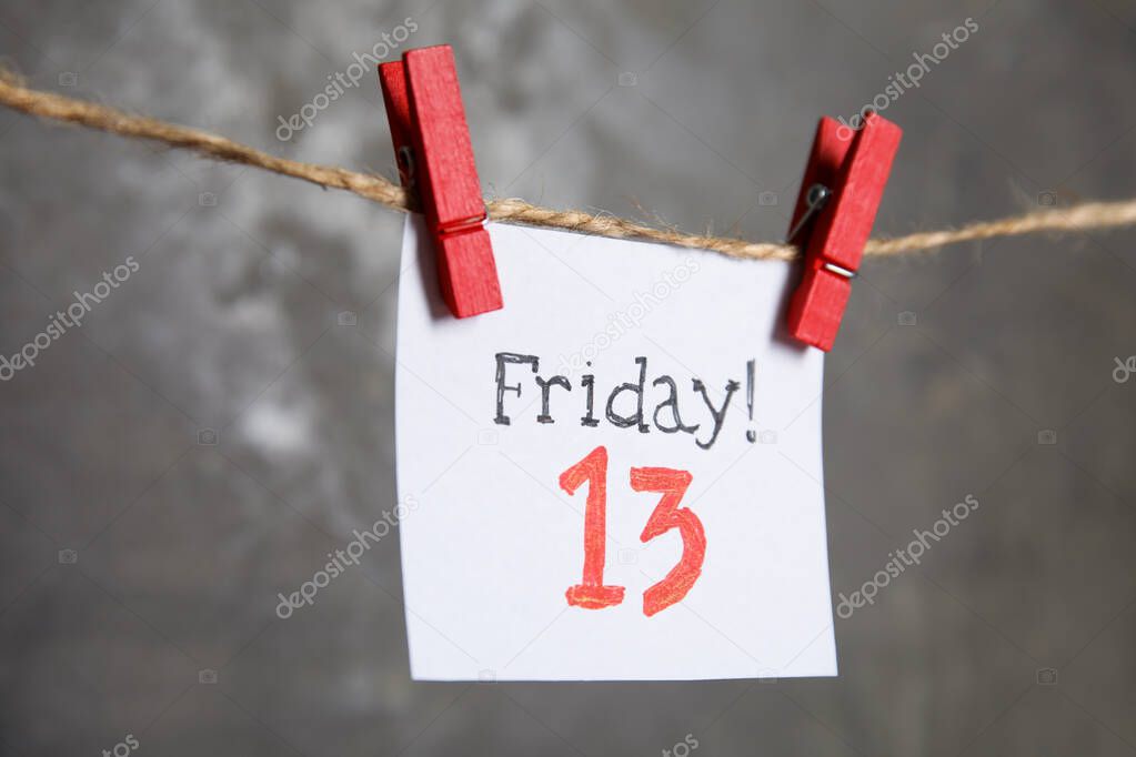 Paper note with phrase Friday! 13 hanging on twine against grey background. Bad luck superstition