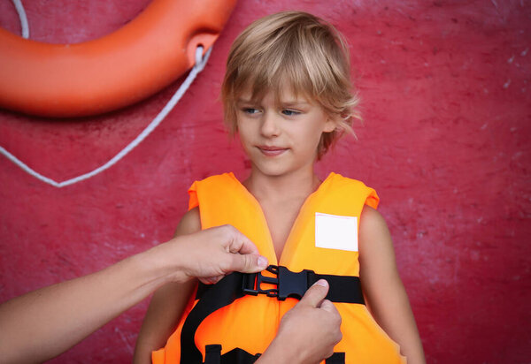 Rescuer putting orange life vest on child near red wall