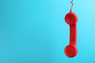 Açık mavi arkaplanda asılı kırmızı kablolu telefon ahizesi, mesaj için boşluk. Yardım hattı kavramı