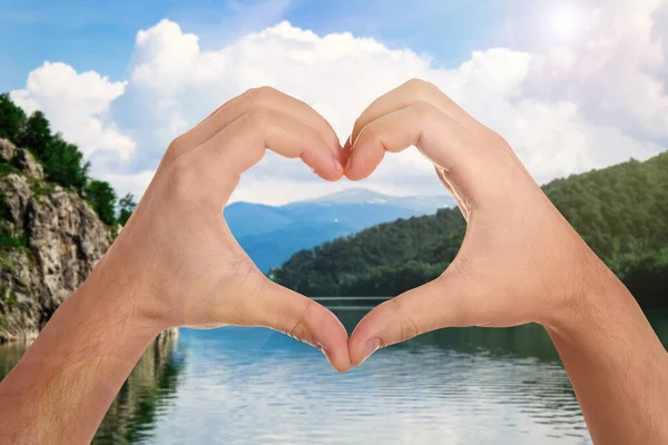 Man making heart with hands near lake on sunny day, closeup