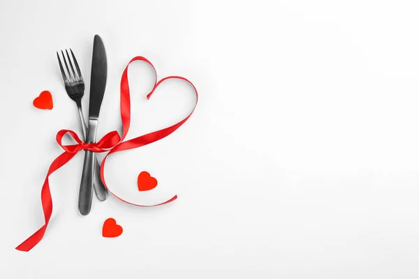 Beautiful cutlery set, hearts and red ribbon on white background, flat lay with space for text. Valentine\'s Day dinner