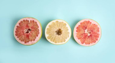 Açık mavi arka planda taze kesilmiş pomelo meyveleri, düz uzanmış.