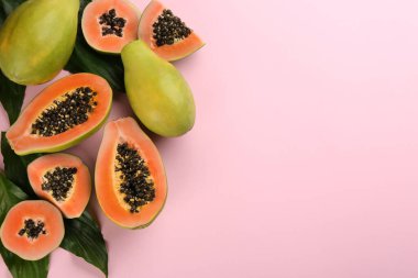 Pembe arka planda yeşil yapraklı taze olgun papaya meyveleri. Metin için boşluk
