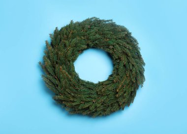 Açık mavi arka planda köknar dallarından yapılmış Noel çelengi, üst manzara