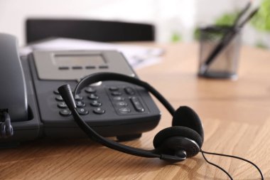 Masaüstü telefonu ve kulaklığı ofisteki ahşap masada, yakın plan. Yardım hattı servisi