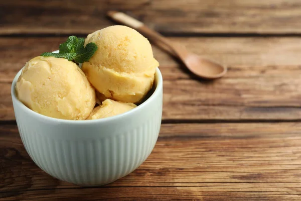 Delicious yellow ice cream in bowl on wooden table, space for text