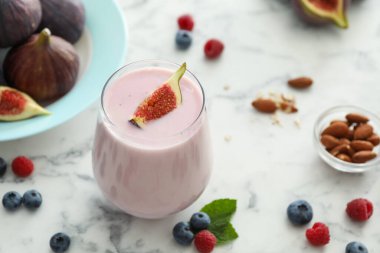 Beyaz mermer masada cam içinde nefis incirli smoothie.