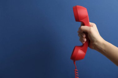 Mavi arka planda kırmızı kablosuz telefonu olan bir kadının yakın görüntüsü, mesaj için yer var. Yardım hattı kavramı