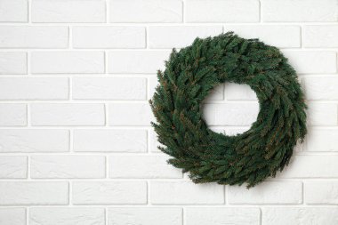 Beyaz tuğla duvardaki köknar dallarından yapılmış Noel çelengi. Metin için boşluk