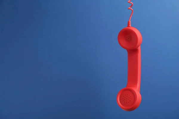 红色带绳电话听筒挂在蓝色背景上 有文字空间 热线电话的概念 — 图库照片