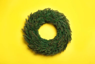 Sarı arka planda köknar dallarından yapılmış Noel çelengi.