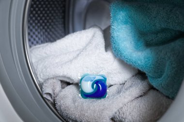 Çamaşır makinesi varilinde çamaşır deterjanı kapsülü ve havlular, yakın çekim görünümü