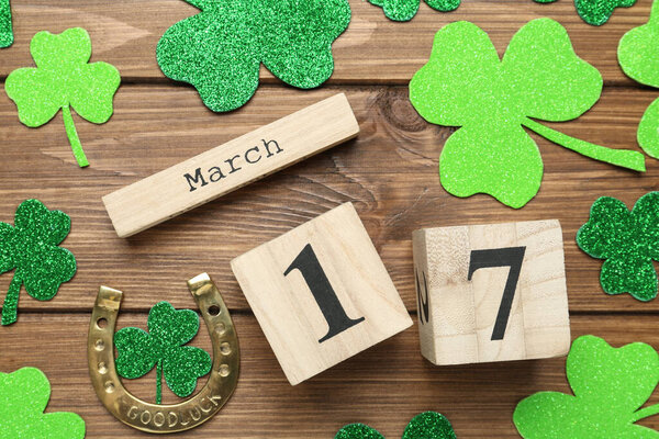 Decorative clover leaves, horseshoe and block calendar on wooden background, flat lay. St. Patrick's Day celebration