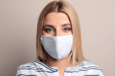 Bej arka planda koruyucu maskeli genç bir kadın.