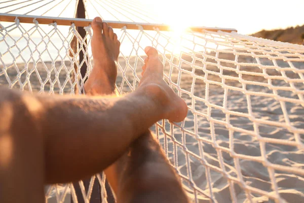 Man relaxing in hammock on beach at sunset, closeup
