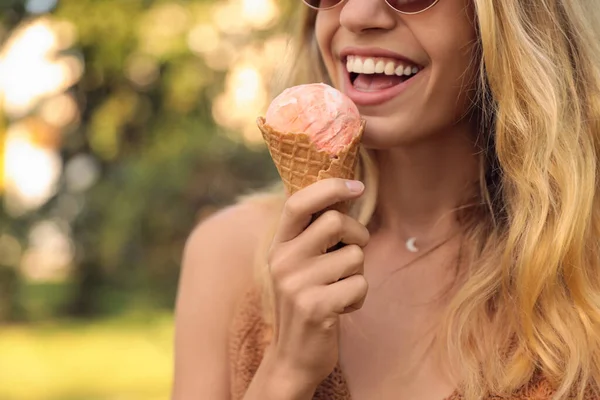 Young woman with delicious ice cream in waffle cone outdoors, closeup