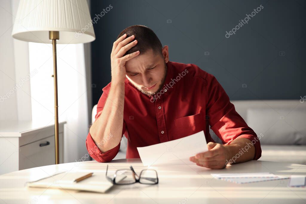 Man reading paper letter at white table in room