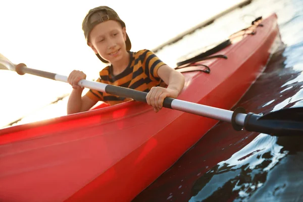 Happy little boy kayaking along river, focus on paddle. Summer camp activity