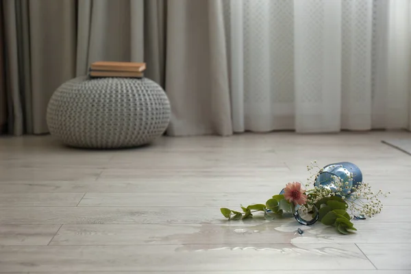 Broken blue glass vase and bouquet on floor in room. Space for text