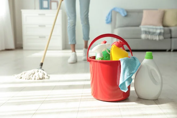 Woman washing floor with mop at home, focus on bucket and cleaning supplies