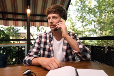 Açık kafede telefonda konuşan yakışıklı bir adam.