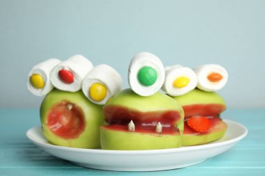 Açık mavi ahşap masadaki canavarlar gibi süslenmiş lezzetli elmalar. Cadılar Bayramı hediyesi