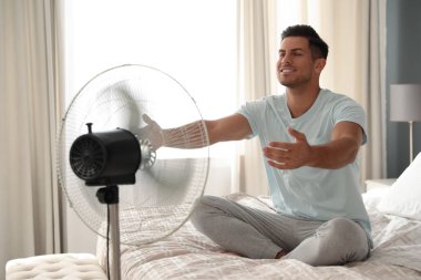 Adam yatakta vantilatörden hava akımının keyfini çıkarıyor. Yaz sıcağı