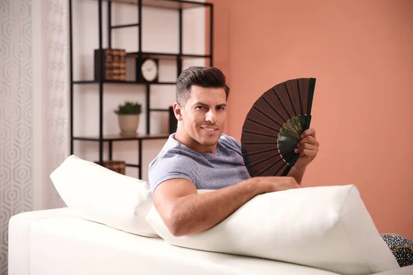 Man with hand fan sitting on sofa. Summer season