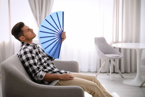 Man with hand fan sitting on sofa. Summer season