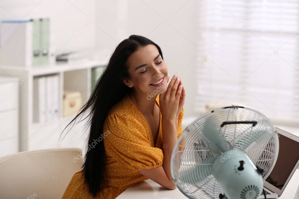Young woman enjoying air flow from fan at workplace