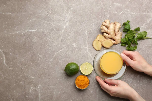 Woman holding cup of immunity boosting drink at table with ingredients, top view. Space for text