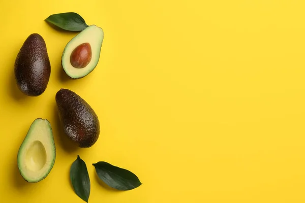 Ganze Und Geschnittene Reife Avocados Mit Grünen Blättern Auf Gelbem — Stockfoto