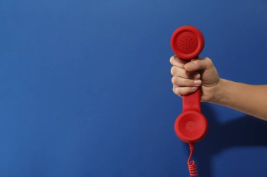 Mavi arka planda kırmızı kablosuz telefonu olan bir kadının yakın görüntüsü, mesaj için yer var. Yardım hattı kavramı
