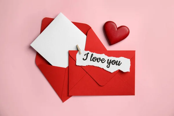 Sheet of paper with phrase I Love You, envelopes and decorative heart on pink background, flat lay