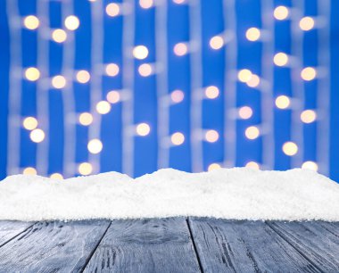 Tahta yüzey karla kaplı ve arka planda bulanık Noel ışıkları, bokeh etkisi 