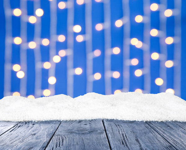 Wooden surface with heap of snow and blurred Christmas lights on background, bokeh effect 