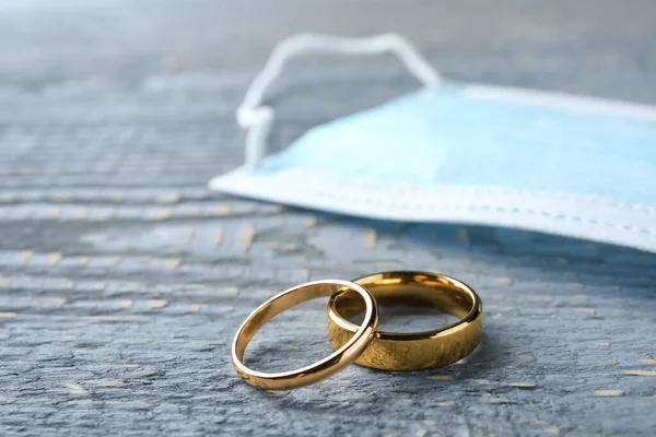 Wedding rings and protective mask on grey wooden table, space for text. Divorce during coronavirus quarantine